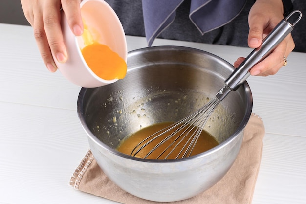 Female hands pour melted butter from a white bowl into crumbled biscuits while making a homemade dessert.