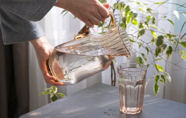 female hands pour water from a decanter into a transparent glass