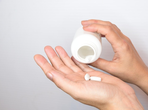 Female hands pouring vitamins from a white jar into the palm