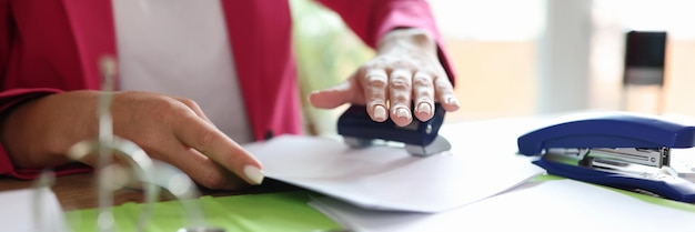 Photo female hands punching holes with puncher in documents in office stationery concept