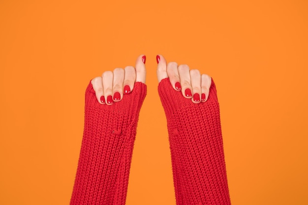 Female hands raised up on orange background Red sweater and red fingernails Freedom symbol