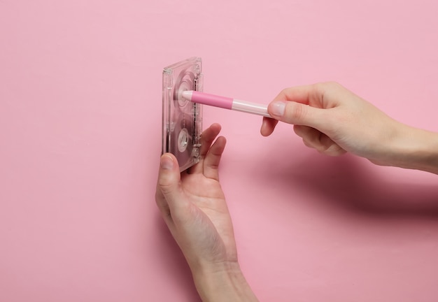 Female hands rewind an audio cassette tape on a pink pastel background