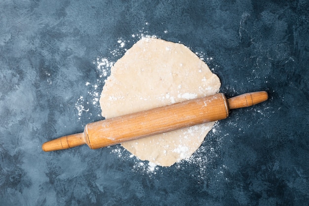 Female hands rolling dough on a table with a wooden rolling pin.