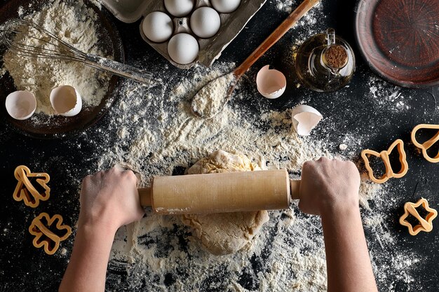 Mani femminili che rotolano la pasta con un mattarello su un tavolo nero vista dall'alto