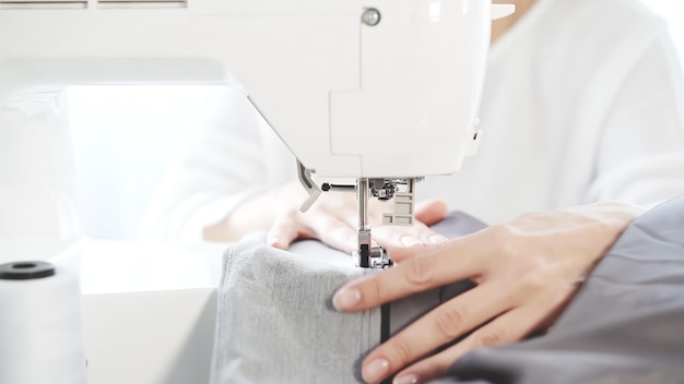 Female hands sew on a white sewing machine closeup