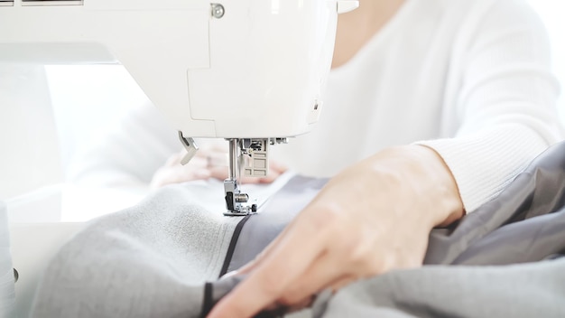 Female hands sewing grey cloth on a white sewing machine closeup