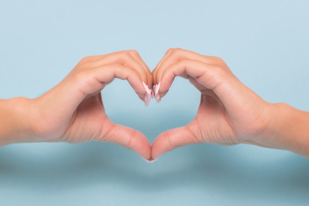 Female hands in shape of heart on blue background