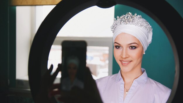 Female hands shooting on smartphone happy muslim bride with professional make up and tiara