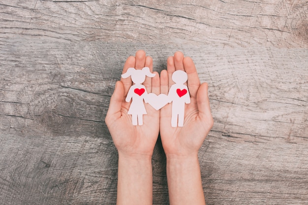 Female hands show two paper people, a man and a woman, on a wooden background