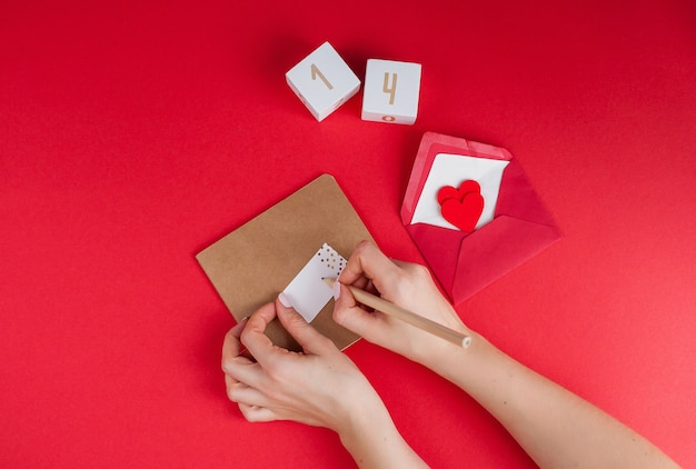 Female hands sign a card. Valentine's day concept. Valentine, hearts, pencil, wooden cubes with number 14 of February