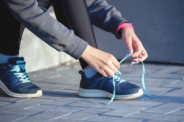 街でのウォームアップ後、スポーツウェアの女性の手が階段のスニーカーに靴ひもを結ぶ