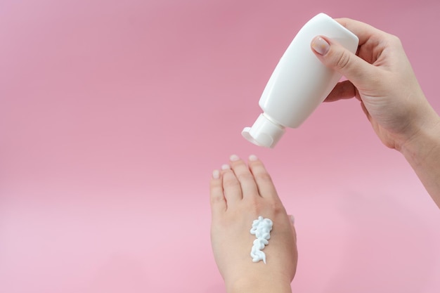 Женские руки выжимают крем из тюбика на розовом фоне Sosmetic бутылки для косметических или медицинских товаров
