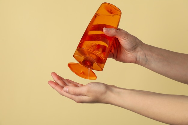 Female hands squeezing shampoo from bottle on beige background