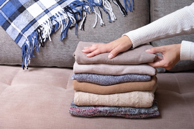 Female hands stack cozy knitted sweaters on the sofa Warm concept