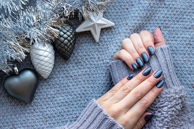 Female hands in sweater with blue glittered nails