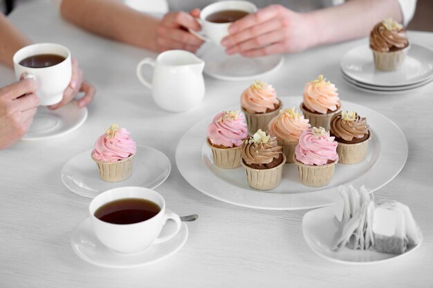 Female hands at the table with tea and cupcakes closeup