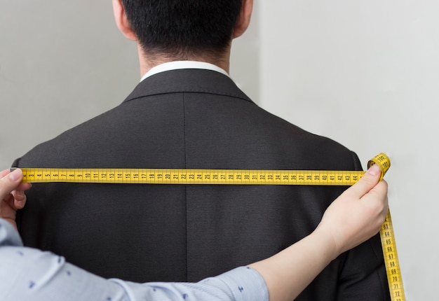 Female hands take measurements from the jacket with a striking ribbon, rear view, close-up