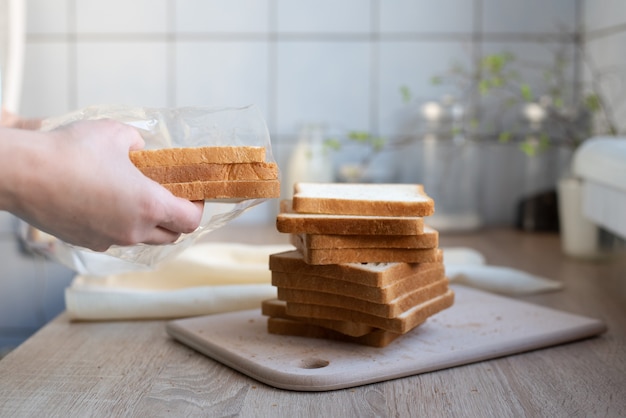 Женские руки вынимают кусочки хлеба из пакета на кухонном столе