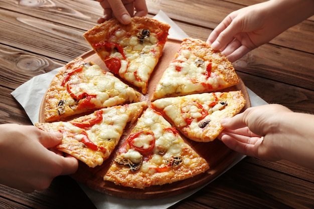 Female hands taking pizza slices on wooden table