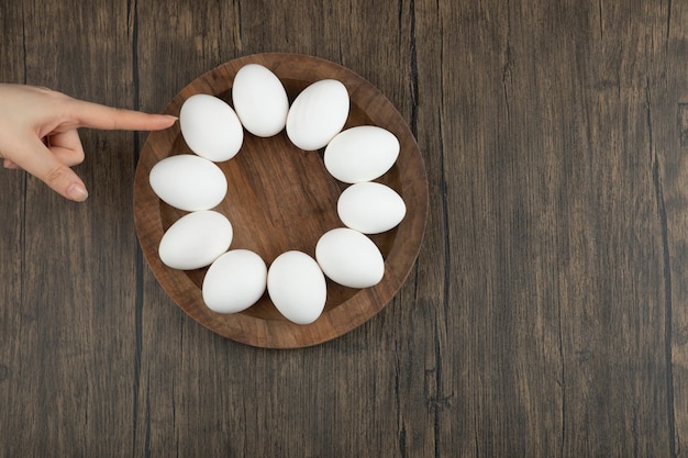 Mani femminili che toccano la tavola di legno con le uova crude su una superficie di legno.