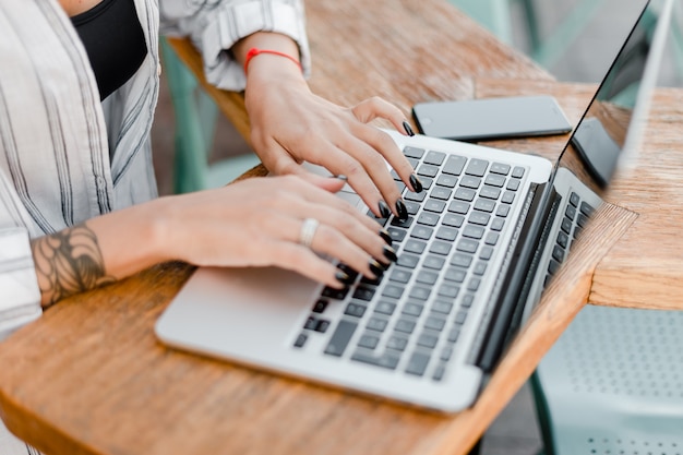 Mani femminili che scrivono sulla tastiera del computer portatile nel caffè