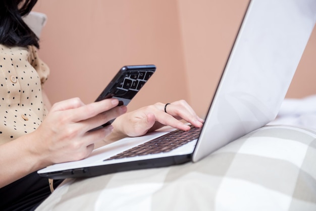 Female hands typing on laptop keyboard while holding cell phone