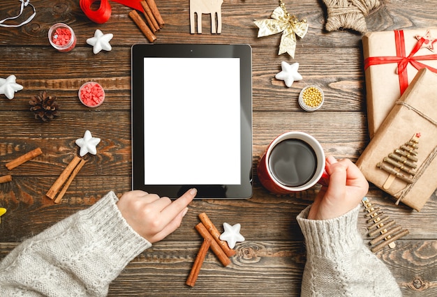 Female hands uses a tablet, sitting at a table with Christmas accessories