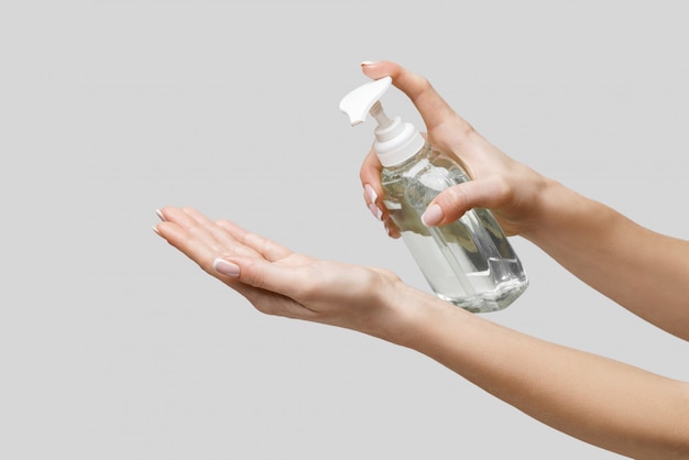 Female hands using hand sanitizer gel or liquid soap dispenser over light grey wall