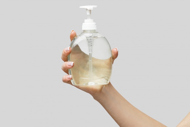 Female hands using hand sanitizer gel or liquid soap dispenser over light grey wall