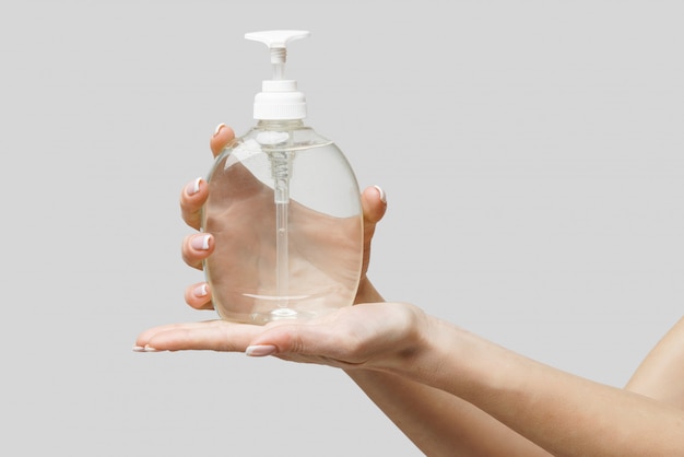 female hands using hand sanitizer gel or liquid soap dispenser over light grey wall