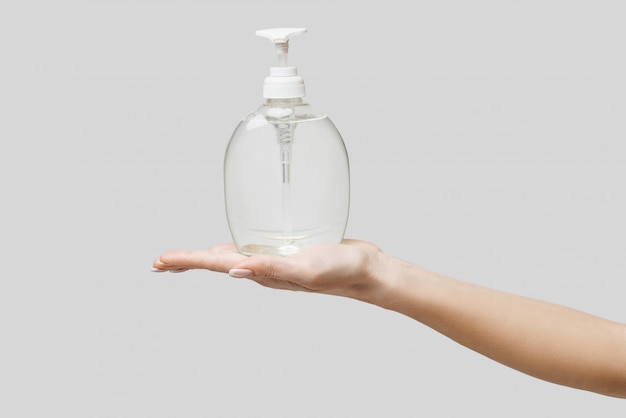 Female hands using hand sanitizer gel or liquid soap dispenser over light grey wall