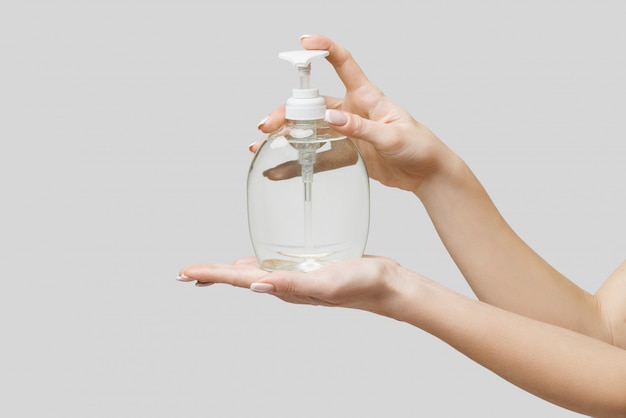 Female hands using hand sanitizer gel or liquid soap dispenser over light grey wall