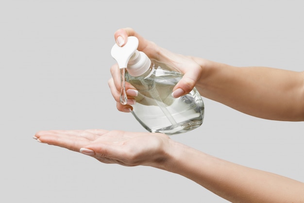 Female hands using hand sanitizer gel or liquid soap dispenser over light grey wall