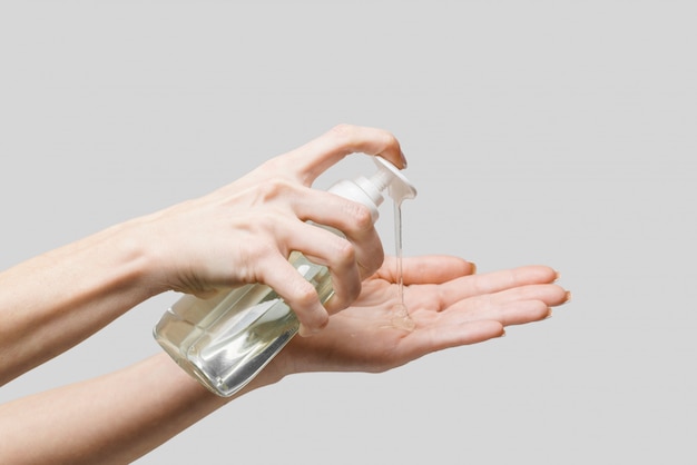 Female hands using hand sanitizer gel or liquid soap dispenser over light grey wall