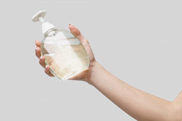 female hands using hand sanitizer gel or liquid soap dispenser over light grey wall