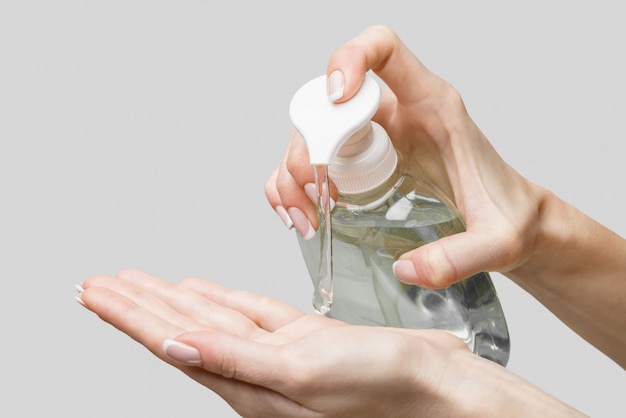 Female hands using hand sanitizer gel or liquid soap dispenser over light grey wall