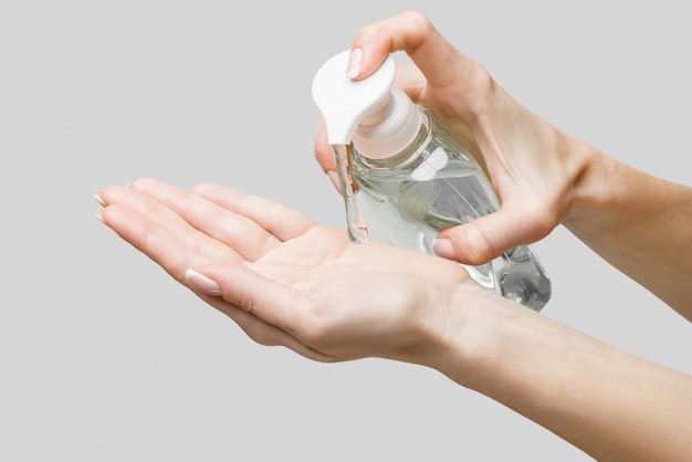 Female hands using hand sanitizer gel or liquid soap dispenser over light grey wall