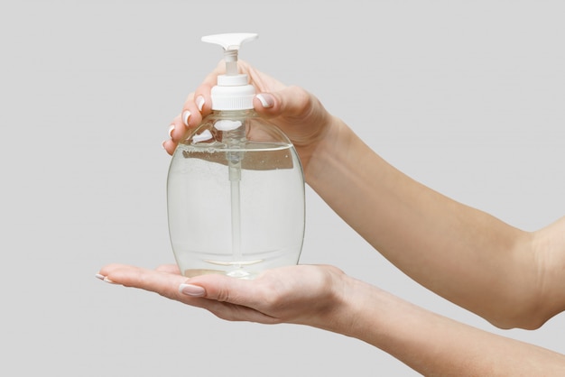 Female hands using hand sanitizer gel or liquid soap dispenser over light grey wall