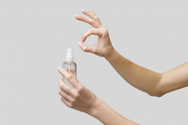 Female hands using hand sanitizer spray dispenser over light grey wall