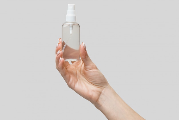 Female hands using hand sanitizer spray dispenser over light grey wall