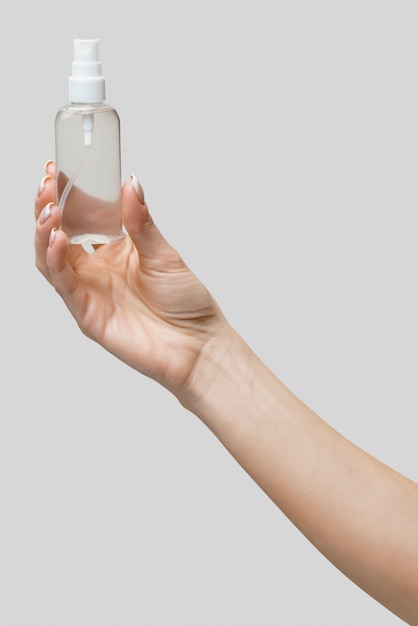 Female hands using hand sanitizer spray dispenser over light grey wall