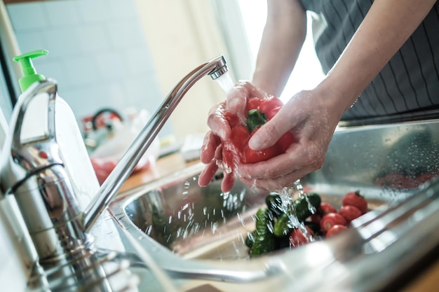 女性の手は水の流れの下で赤唐辛子を洗う