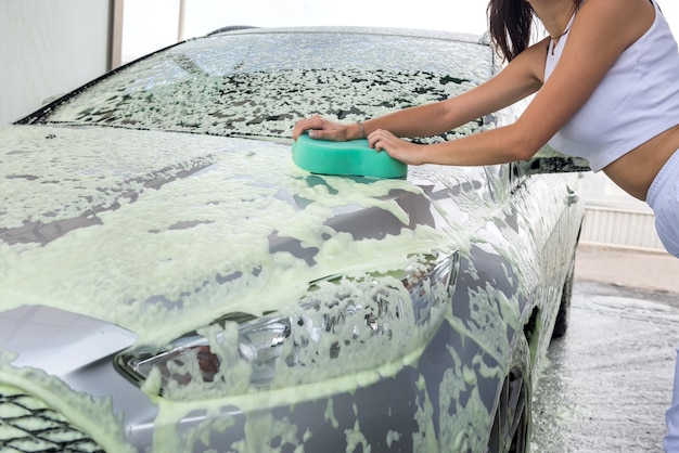 Женские руки моют машину с помощью губки для автомойки с пеной на автомойке