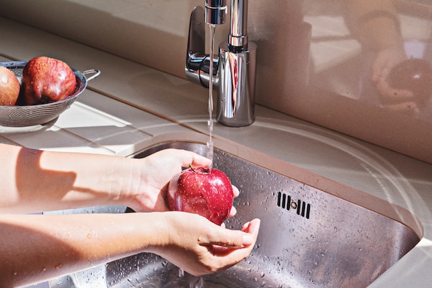 Female hands washing red apple in sink