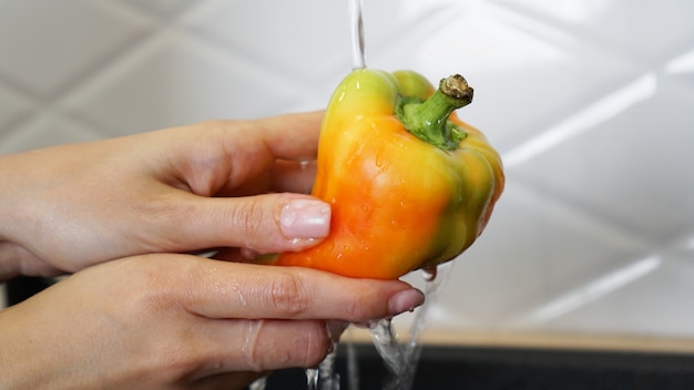 Photo female hands washing yellow and red color pepper.