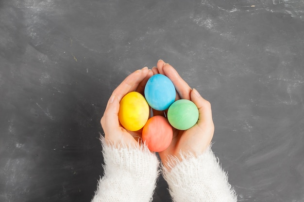 Le mani femminili in un maglione lanuginoso bianco tengono le uova di pasqua colorate sopra una lavagna