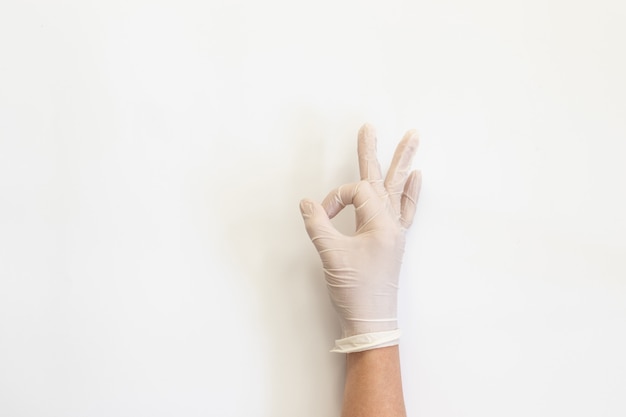 Mani femminili in guanti medici bianchi che mostrano segno giusto.