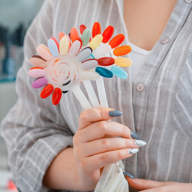 사진 인공 아크릴 손톱을 가진 여성의 손은 매니큐어 디자인을 위한 새로운 폴란드어 색상을 선택합니다. 미용실에서 손톱을 색칠하기 위한 다양한 매니큐어