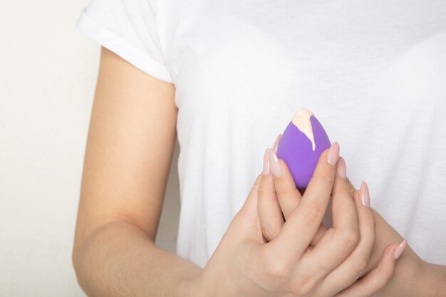 Female hands with beautiful manicure holding purple beauty blender with liquid foundation