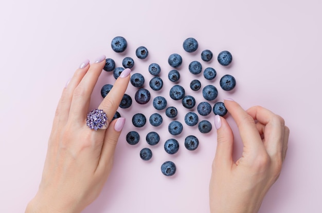 Female hands with beautiful manicure making heart shape with blueberries